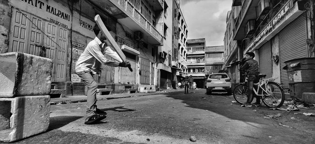 Monochrome photo of kids playing cricket in a Jaipur street, capturing urban life.